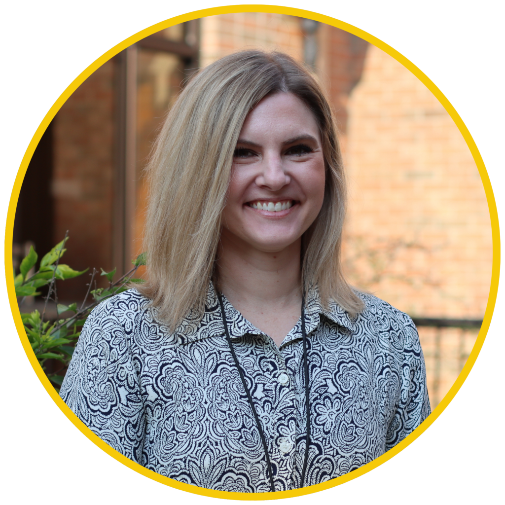 A smiling woman with blonde hair wearing a patterned black and white shirt stands outdoors, framed in a circular yellow border.